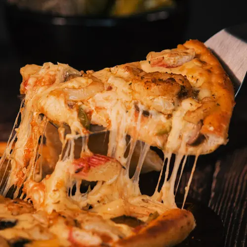 A cheesy slice of pizza being lifted from the whole pie, with toppings including melted cheese.