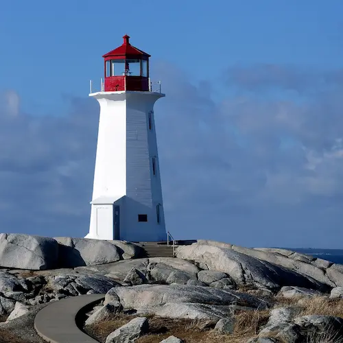A tall white lighthouse perched on rugged, rocky cliffs, overlooking the calm ocean under a clear sky