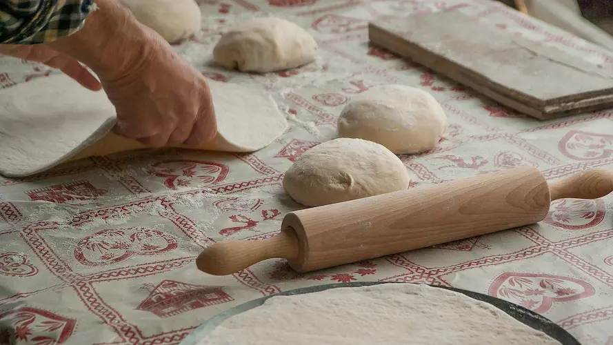Hands preparing pizza dough on a table with rolling pin and dough balls