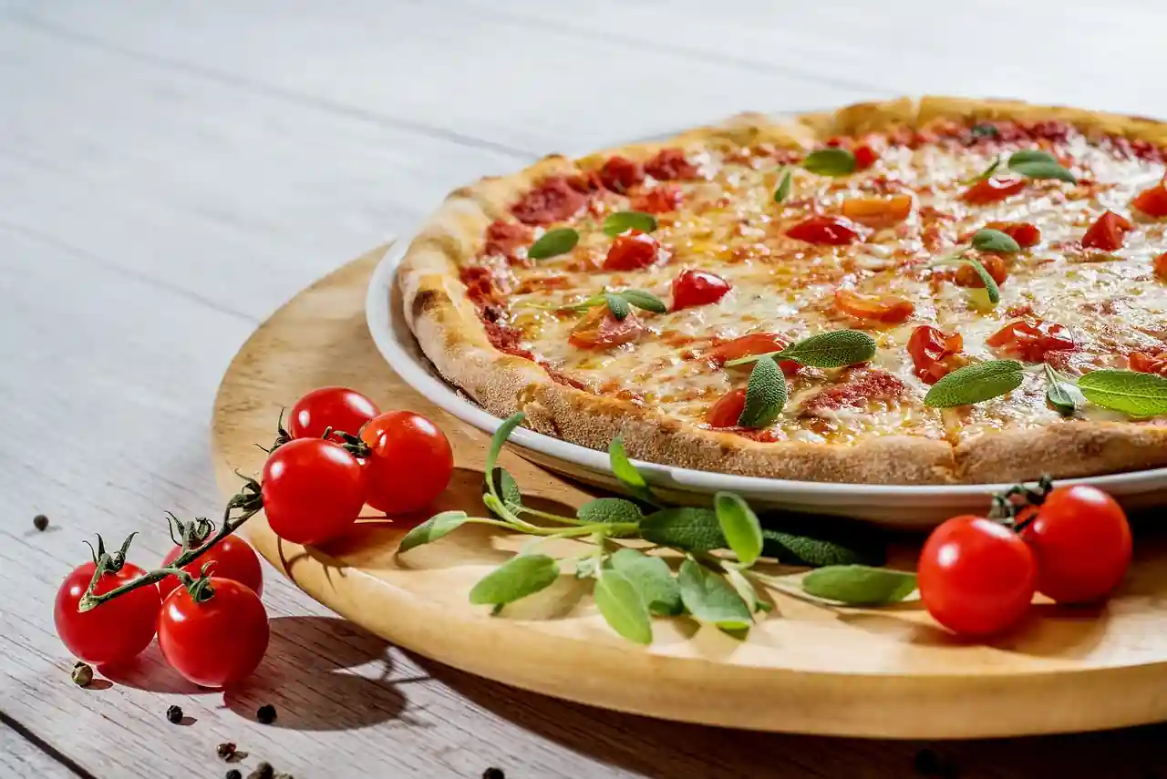 A pizza on a wooden plate garnished with fresh cherry tomatoes and herbs on a white table