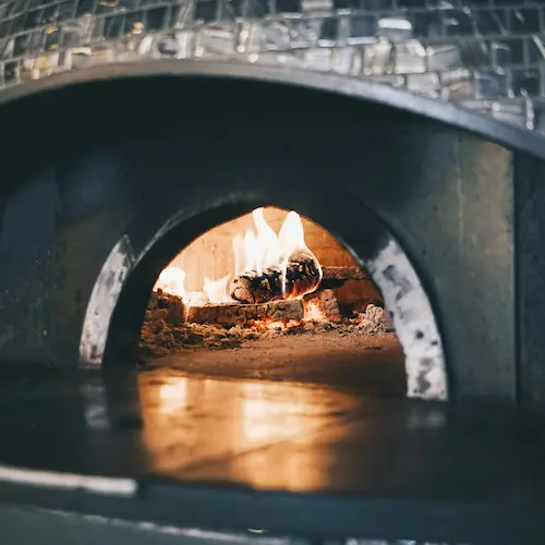 A traditional stone pizza oven with wood burning inside and a slight flame reflection on the base