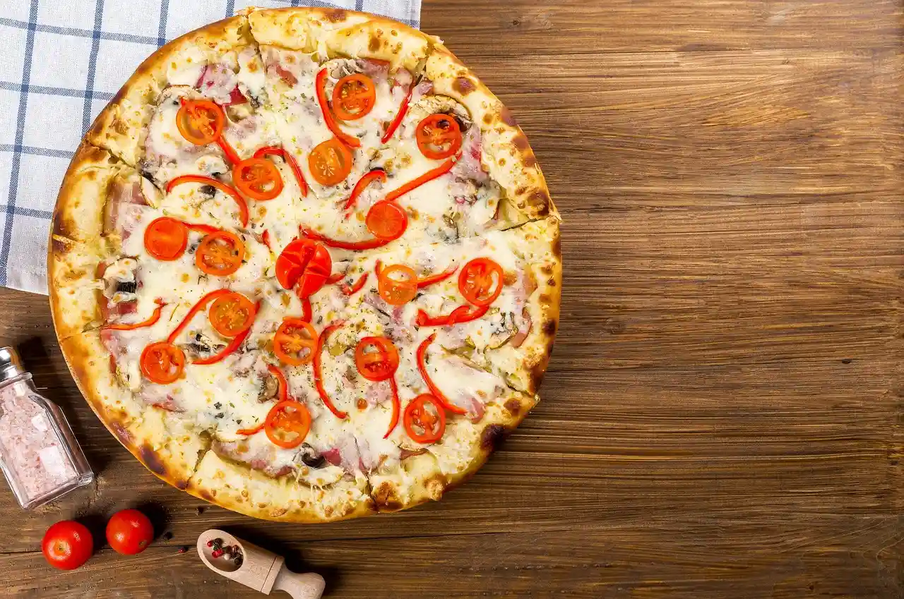 A freshly baked pizza topped with cherry tomatoes and red bell peppers on a wooden table