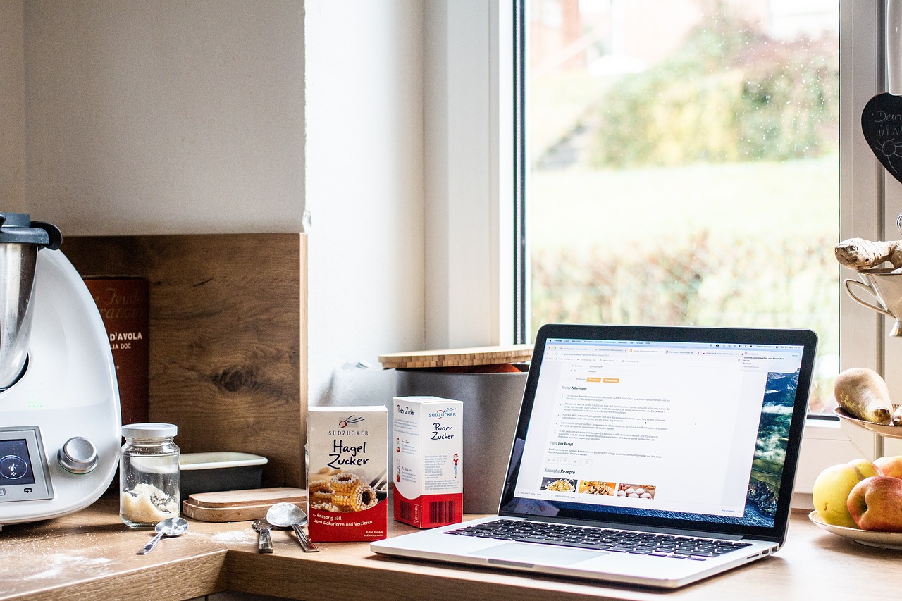 Cozy kitchen scene with baking ingredients, a laptop displaying a recipe, and kitchen tools